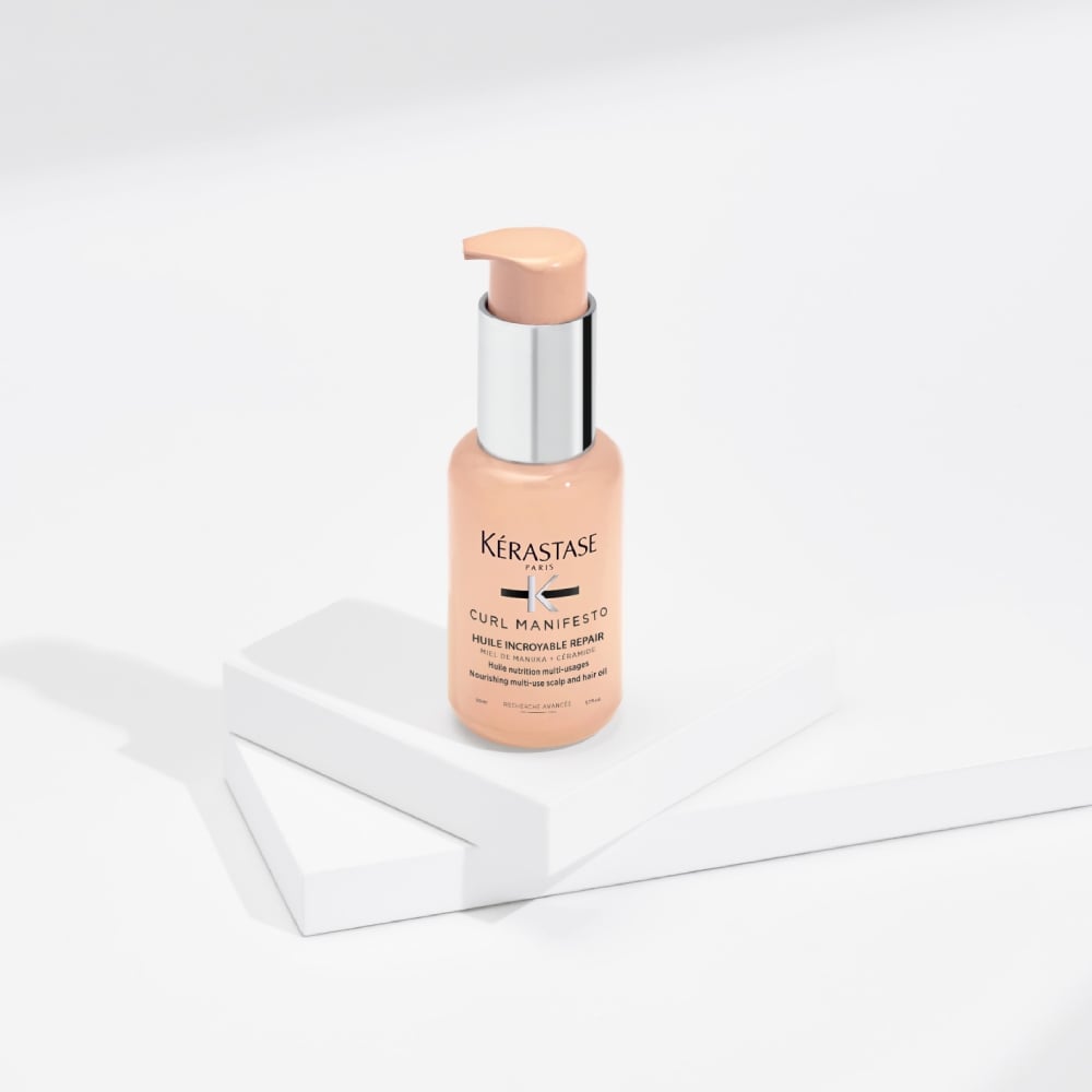 Curl Manifesto Huile Sublime Repair hair oil is displayed on a pure grey background with transparent cubes. This oil hydrates and define the shape of curly hair while reducing frizz and breakage.